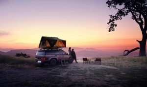 Ein Paar entspannt sich beim Sonnenuntergang mit dem SUV-Zelt auf dem Campingplatz mit Blick auf die Berge.